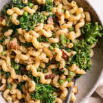 a close up of a bowl of garlicky kale pasta with a fork in the bowl and a linen napkin beside it