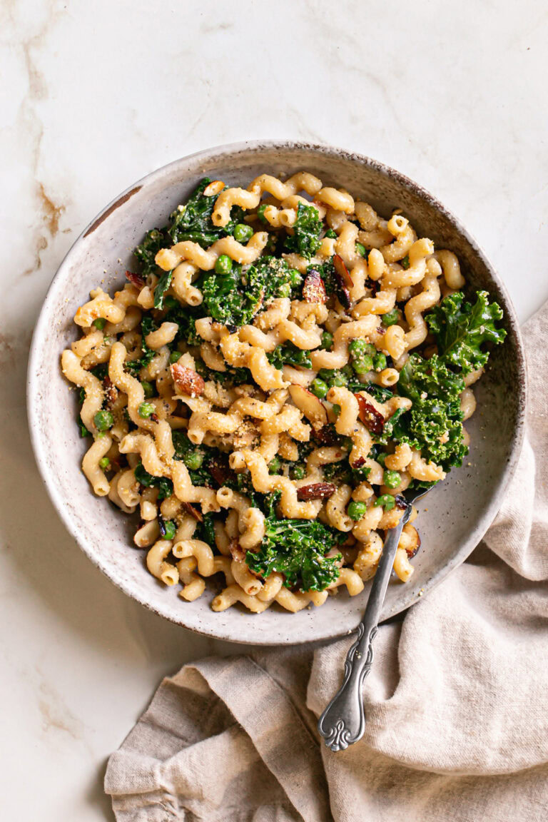 a bowl of garlicky kale pasta with a fork in the bowl and a linen napkin beside it