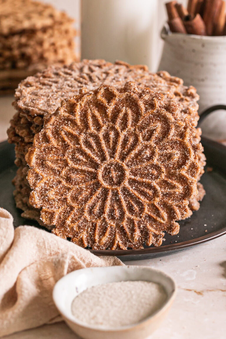 close up of a cinnamon sugar pizzelle leaning against the stack of pizzelles