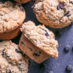 blueberry muffins on a blueberry colored backdrop with fresh blueberries around the muffins