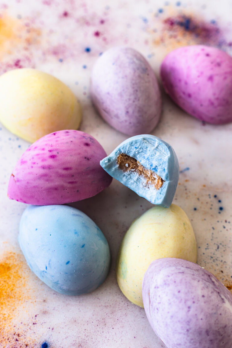 white chocolate colored eggs stacked on top of each other, one with a bite taken out of it to reveal the peanut butter filling
