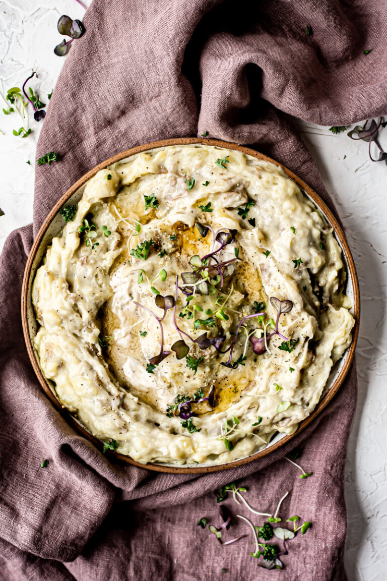 a bowl of mashed potatoes with melted butter garnished with micro greens on top of a purple linen towel