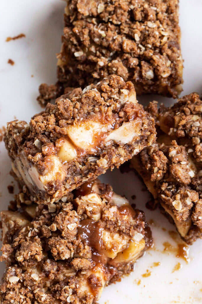 caramel apple crumb bars piled on top of one another with one bar showing the middle layer
