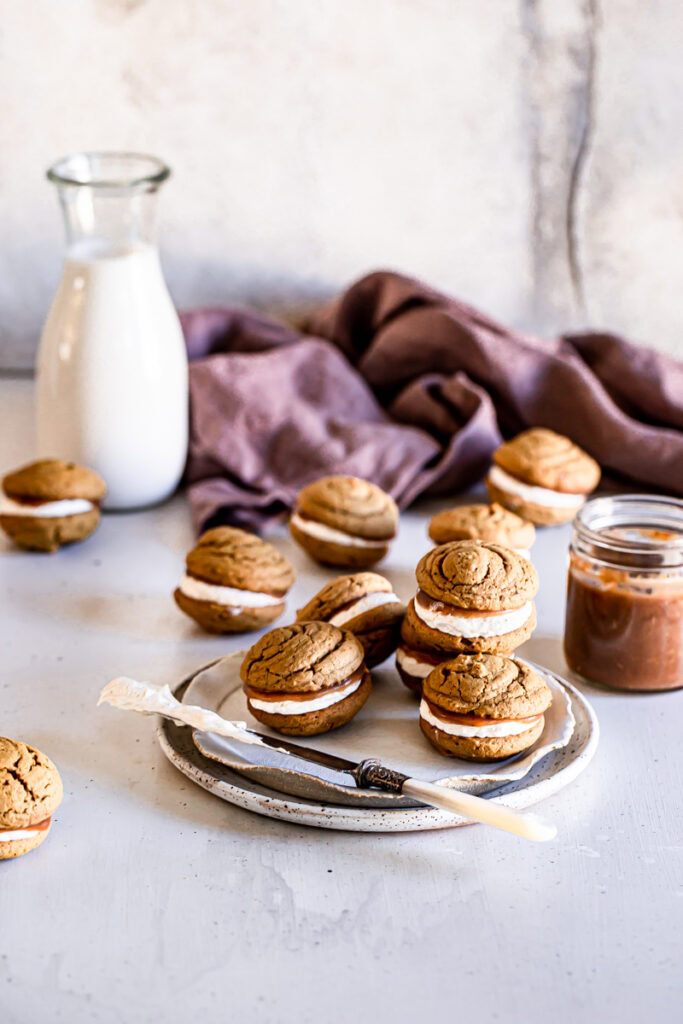 whoopie pies on a plate with a jug of almond milk and jar of apple butter