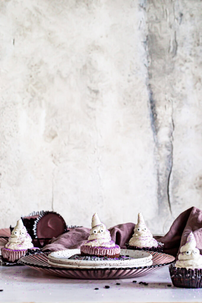 a far away image of mini cheesecake cups with buttercream ghosts on top and a purple linen towel in the background