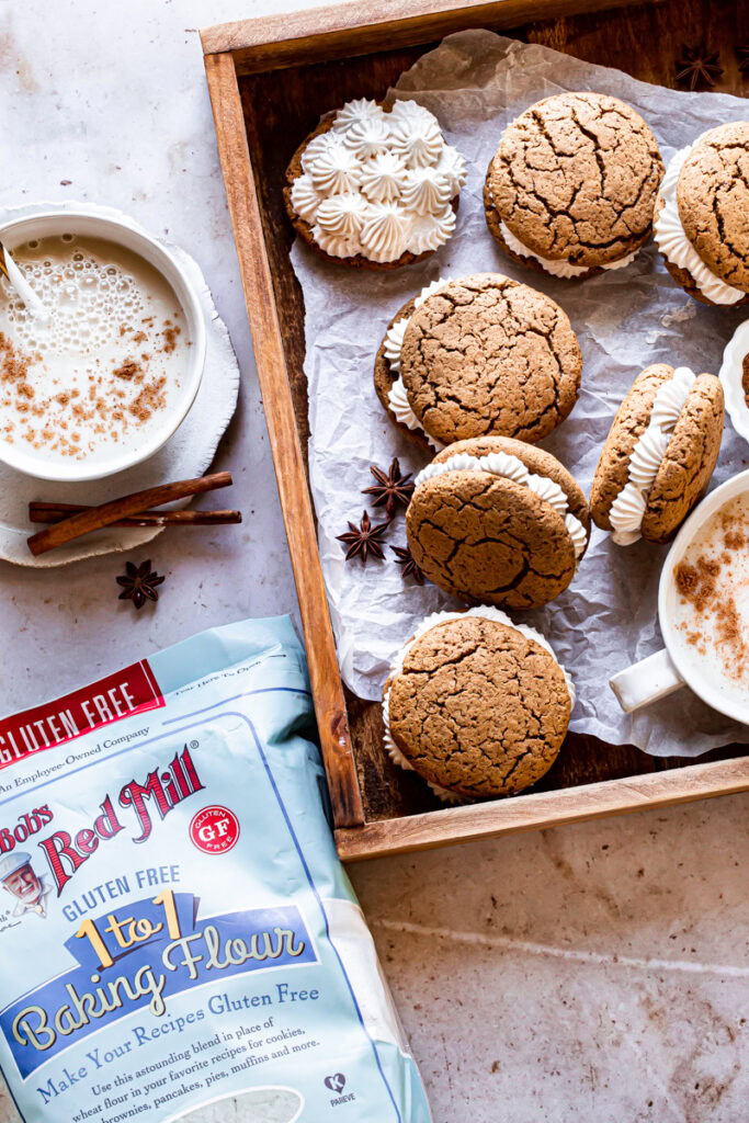 a wooden box with a mug of dairy free egg nog, 6 gingerbread sandwich cookies and a bag of Bob's Red Mill baking flour.