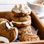 three gingerbread sandwich cookies stacked on top of one another, the top one showing the piped buttercream filling
