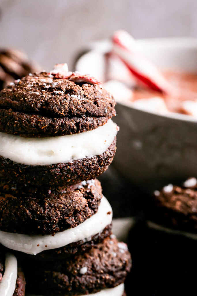 close up shot of hot cocoa Whoopie pies with a cup of hot cocoa in the background