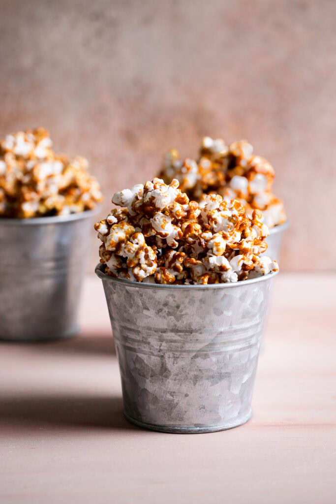 three buckets of caramel popcorn, one in the foreground and two blurred in the back