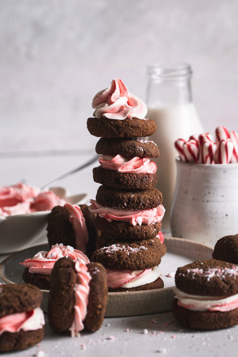 a stack of peppermint cream sandwich cookies with a jar of almond milk and candy cane sticks in the background
