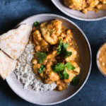 two bowls of rice with breaded cauliflower tossed in a vegan Indian butter sauce garnished with fresh cilantro and a side serving of naan