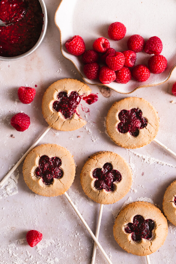 flat lay image of raspberry pie pops with a plate of raspberries and a small saucepan of raspberry preserves