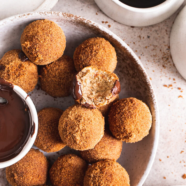 an overhead view of gluten-free, grain free, vegan, naturally sweetened churro donut holes with a bowl of melted chocolate for dipping and one of the donut holes with a bite taken out of it