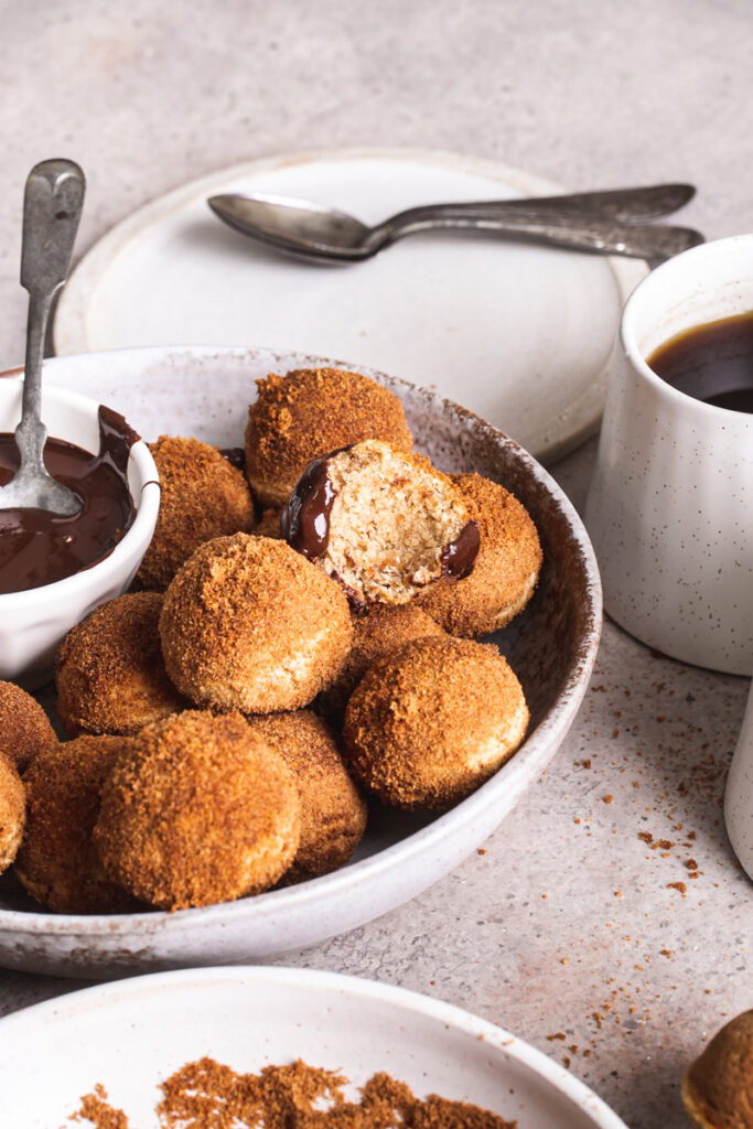 a side view of gluten-free, grain free, vegan, naturally sweetened churro donut holes with a bowl of melted chocolate for dipping and one of the donut holes with a bite taken out of it