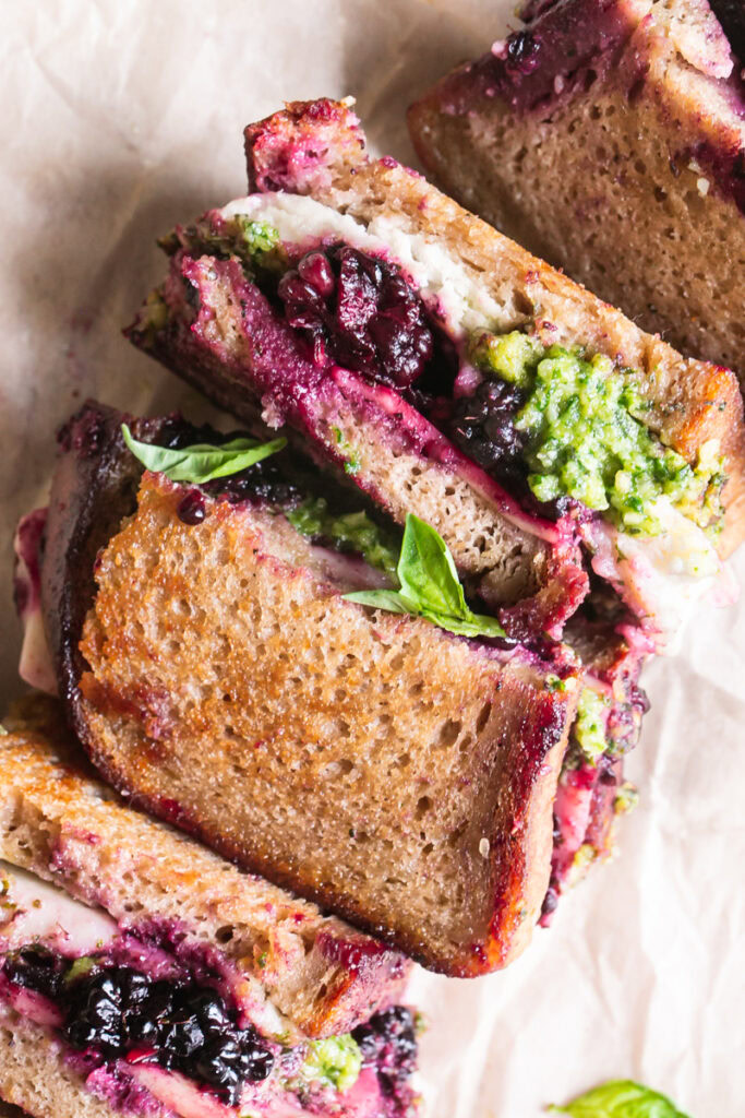a close up image of vegan blackberry pesto grilled cheese sandwich halves on a piece of parchment paper
