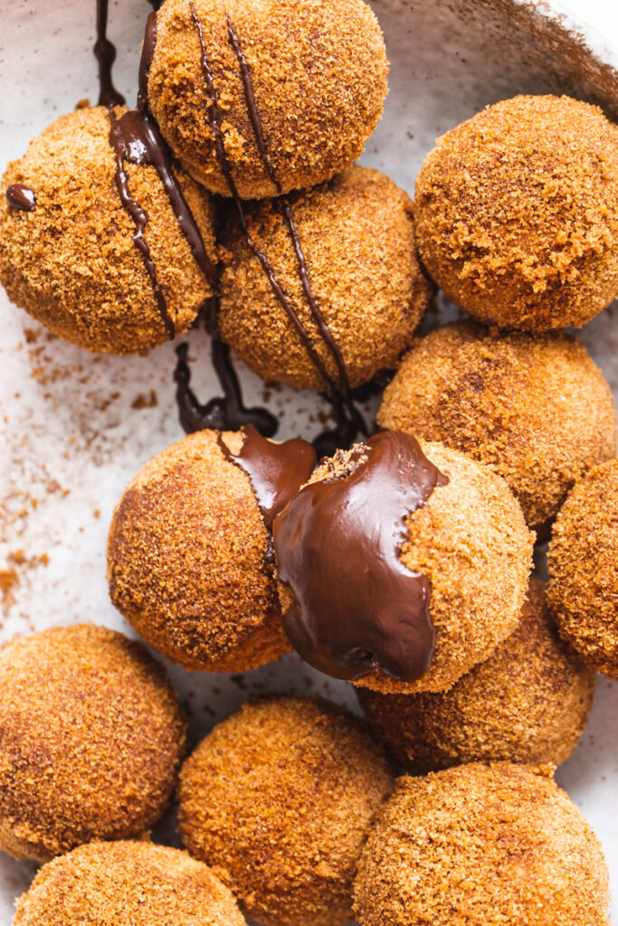 a bowl of grain-free, gluten-free, vegan, naturally sweetened churro donut holes with a bowl of cinnamon coconut sugar beside it with a donut hole in it.