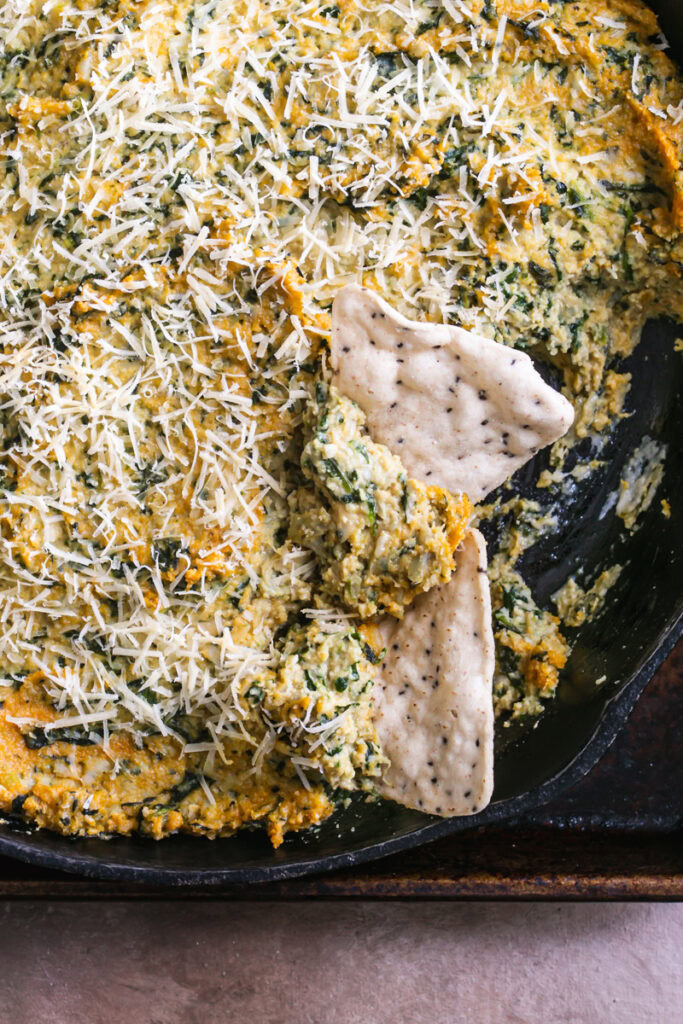 a close up of spinach artichoke dip with 2 tortilla chips