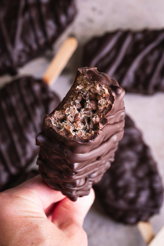 a close up of a single chocolate covered cocoa Krispie crunch pop with a bite taken out of it to show the inside