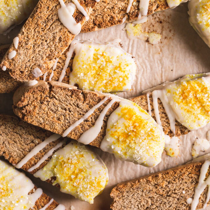 lemon vanilla biscotti piled on top of each other on top of a piece of parchment paper dipped in coconut butter and sprinkled with sparkling sugar and turmeric for color