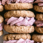 close up flat lay shot of oatmeal sandwich cookies with blackberry cream filling laid in a tray all lined up with the cream filling showing