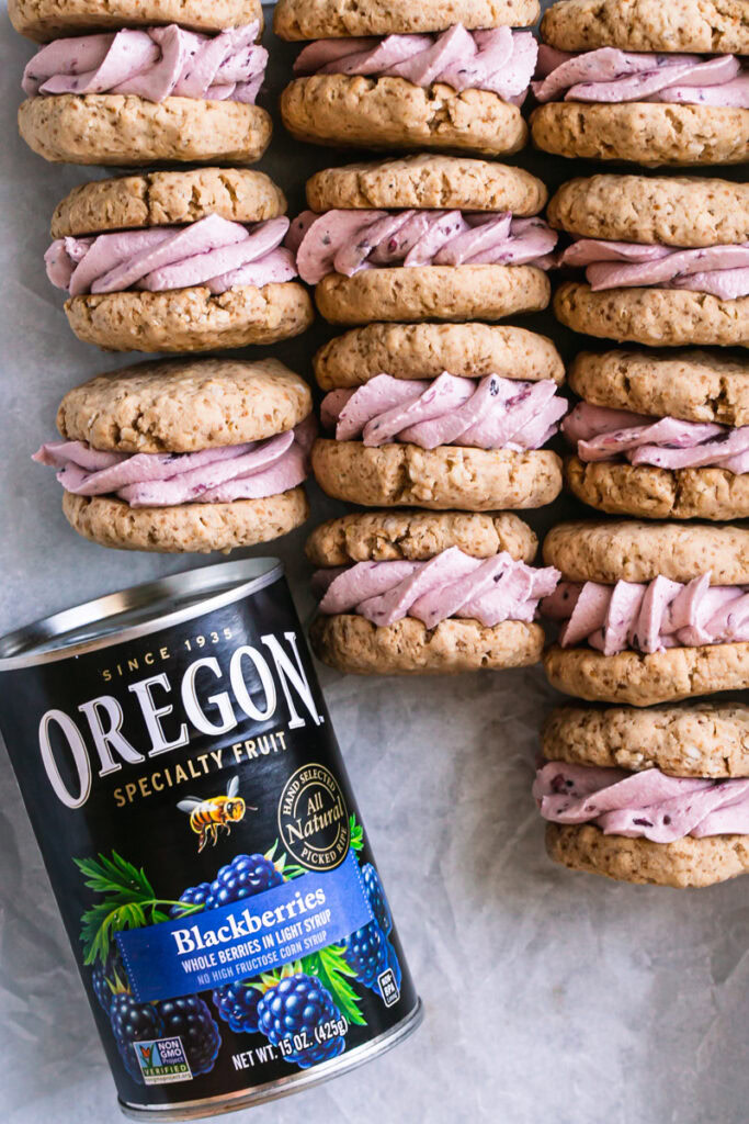 oatmeal sandwich cookies with blackberry cream filling laid in a tray all lined up with the cream filling showing with a can of Oregon canned blackberries in the bottom left corner