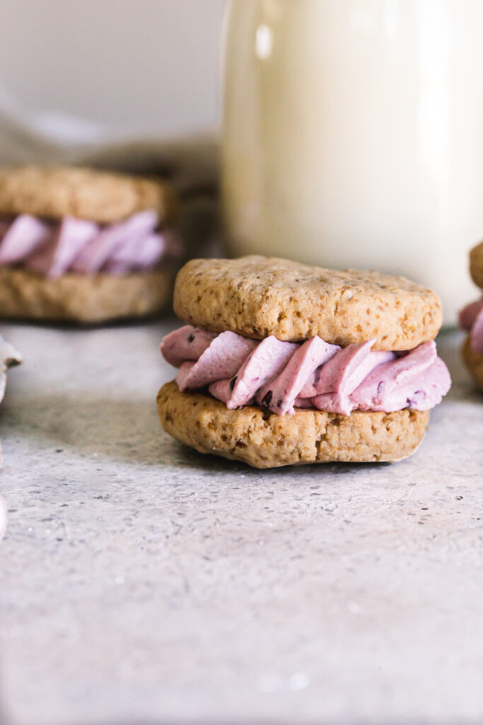a single blackberry oatmeal cream sandwich cookie with a jar of milk in the background