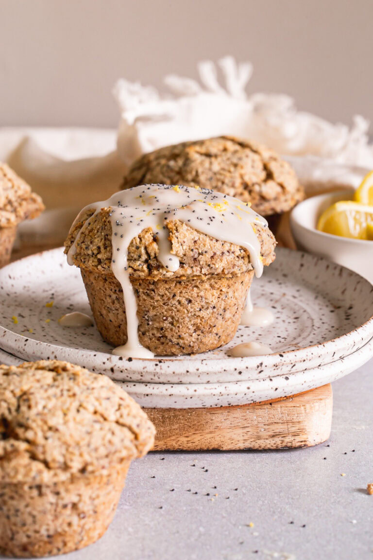 head on shot of lemon poppy seed muffins with one on a plate drizzled with lemon glaze and a bowl of lemons in the background