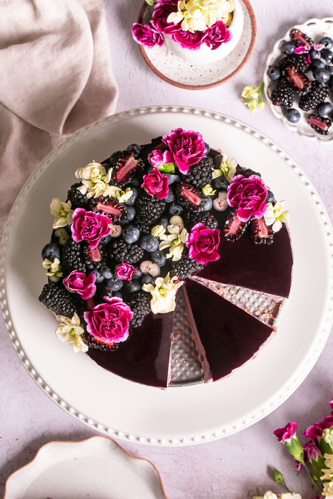haskap berry cheesecake sliced on a cake platter topped with berries and flowers
