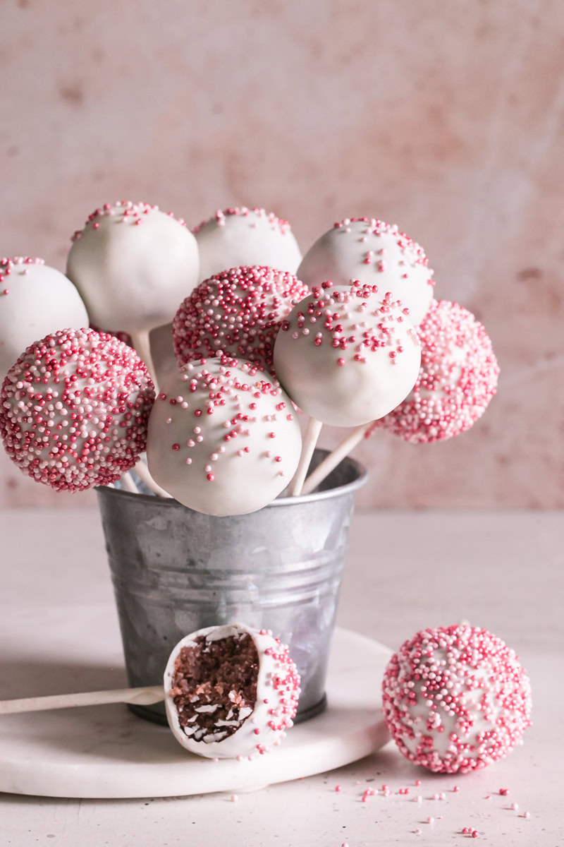 cherry cake pops standing up in a metal bucket one outside of the bucket laying next to it with a bite taken out of it