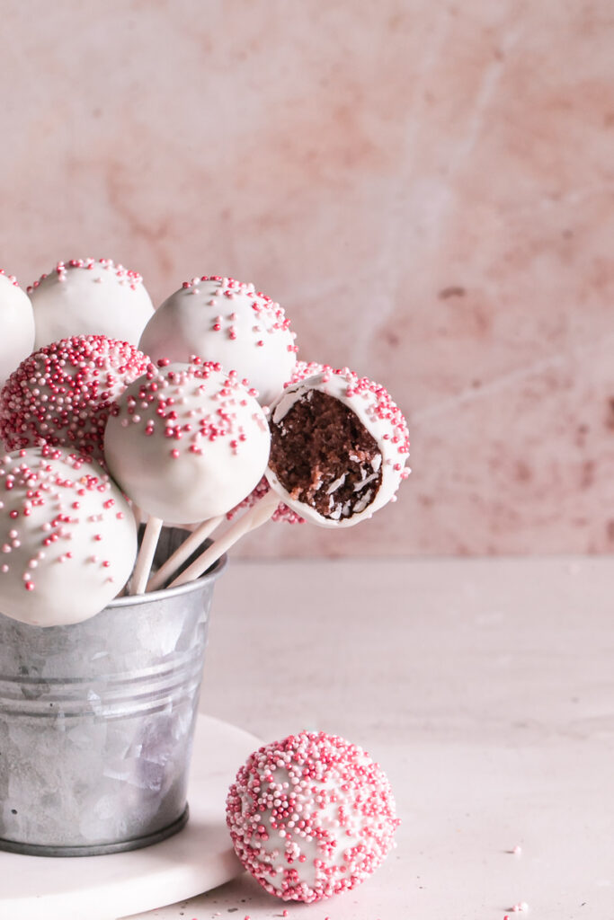 close up shot of cherry cake pops standing up in a metal bucket one with a bite taken out of it