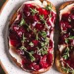 a close up shot of two slices of toast with dairy-free cream cheese, roasted cherries and fresh thyme on a plate