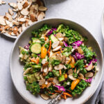 a bowl of Thai chopped salad with a fork in the bowl, a plate of sliced almonds and dressing next to the bowl