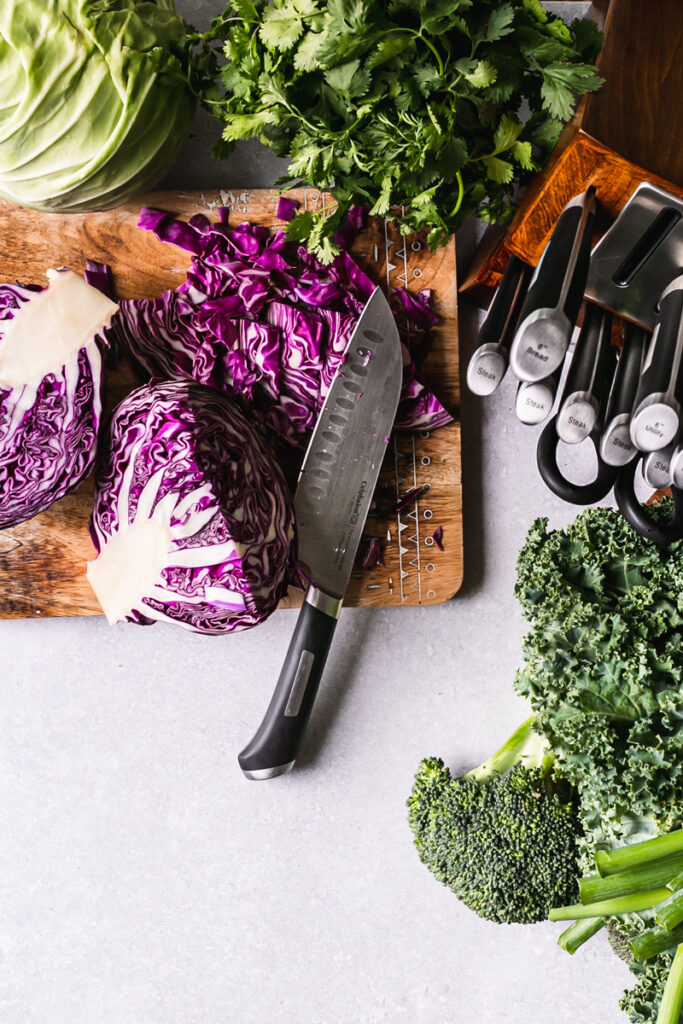 fresh produce on a cutting board with a knife laid out on the cutting board chopping red cabbage and a block of calphalon knives on the side