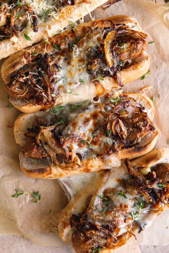 close up of four vegan French onion brats layed out on a parchment line wooden cutting board 