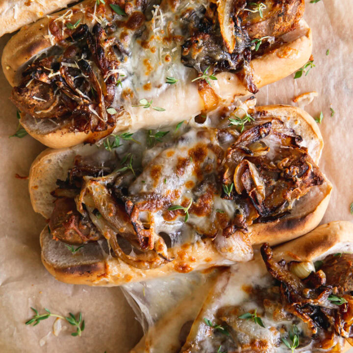 close up of four vegan French onion brats layed out on a parchment line wooden cutting board