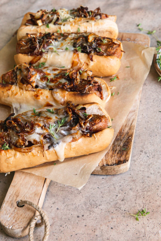 side view of vegan French onion brats on a parchment lined wooden cutting board