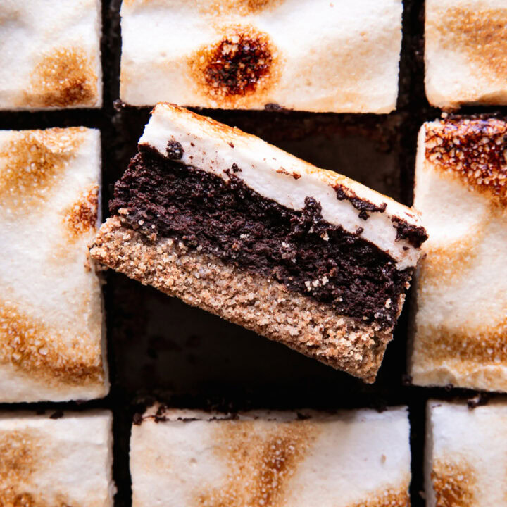 sliced s'mores brownies with toasted marshmallow fluff on top and the middle brownie on its side showing the brownie center and graham-style crust