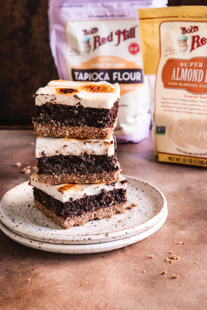 three s'mores brownies stacked on top of one another with a bag of Bob's Red Mill Tapioca Flour and Almond Flour in the background