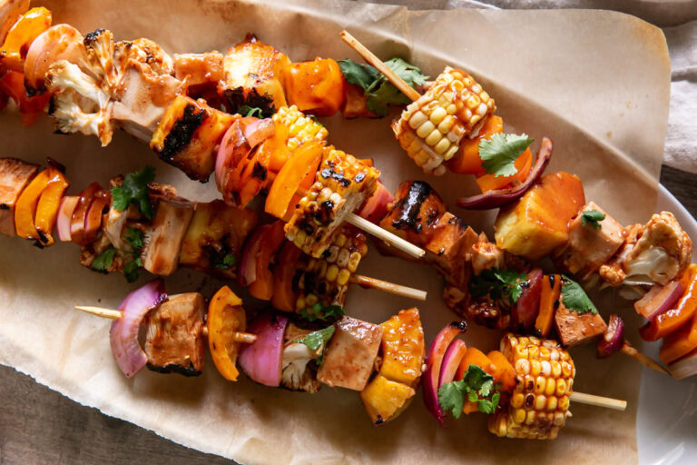 close up of an oval platter with grilled veggie barbecue kabobs on it with a side of barbecue sauce in a bowl beside it and fresh cilantro on a plate above it