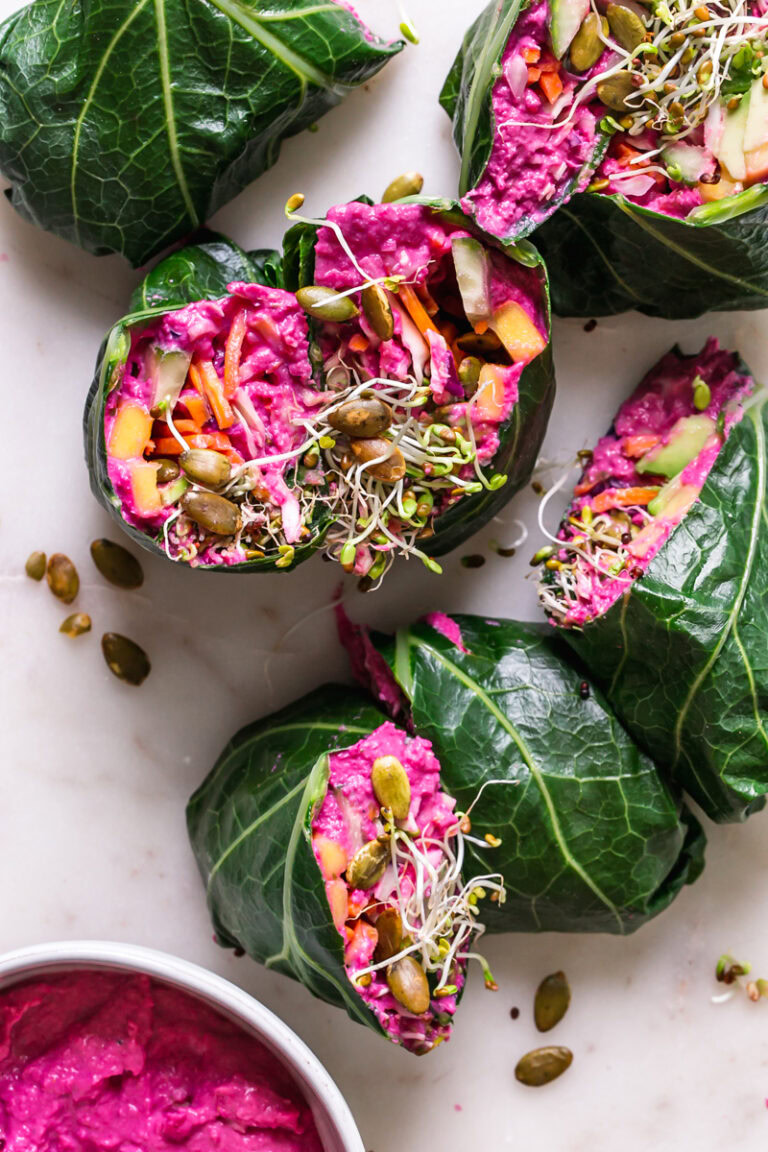 beet hummus veggie collard wraps cut in half with a bowl of beet hummus beside it