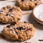 3/4 view of flourless salted tahini chocolate chip cookies with a plate of salt