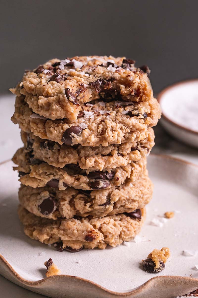 a stack of flourless salted tahini chocolate chip cookies with a bite taken out of the top one