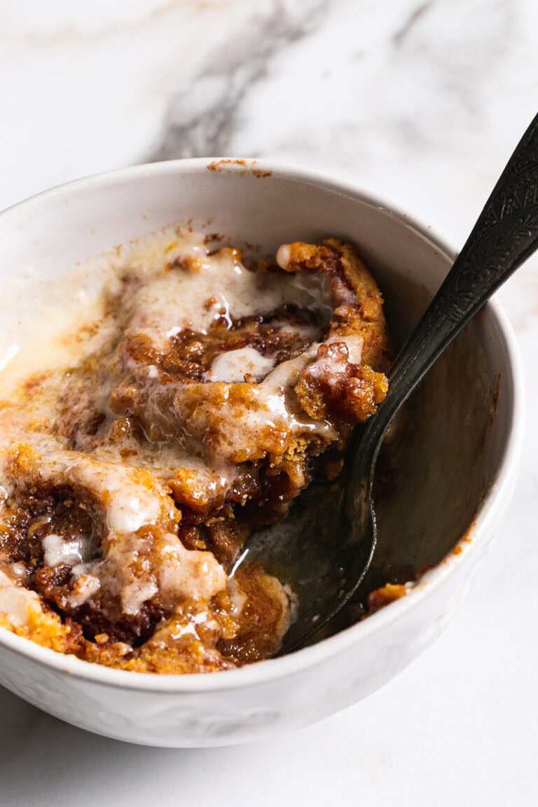 3/4 view of pumpkin cinnamon roll mug cake with a spoon sticking out of it