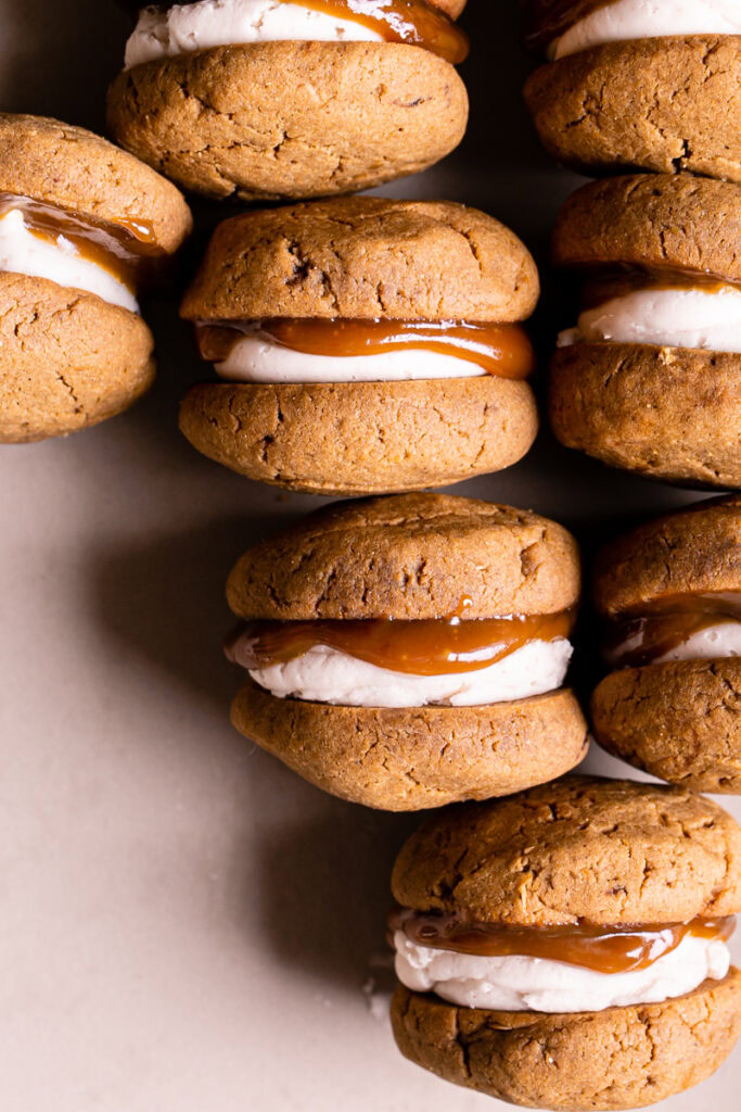 side view of pumpkin spice latte whoopie pies lined up in a row to reveal the butter cream and caramel filling