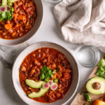 two bowls of chili with two glasses of water and a board of toppings