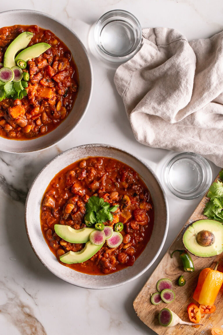 two bowls of chili with two glasses of water and a board of toppings