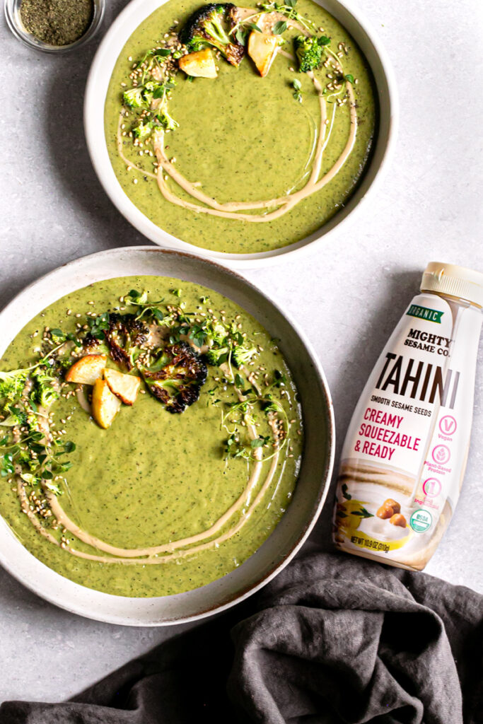 flat lay of two bowls of roasted broccoli potato tahini soup with a bottle of mighty sesame co organic tahini beside it