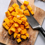 the entire butternut squash cut into chunks on a cutting board with the knife next to it