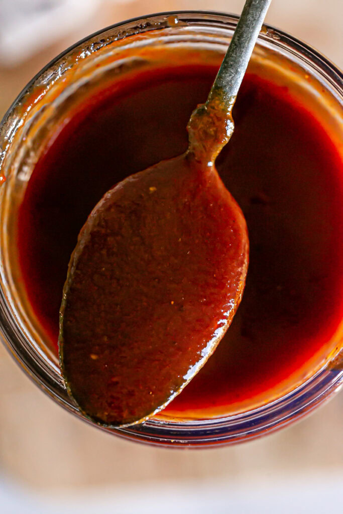 closeup overhead shot of  the spoon with bbq sauce on it resting on the opening of the jar of Gluten-free Vegan Pumpkin BBQ Sauce
