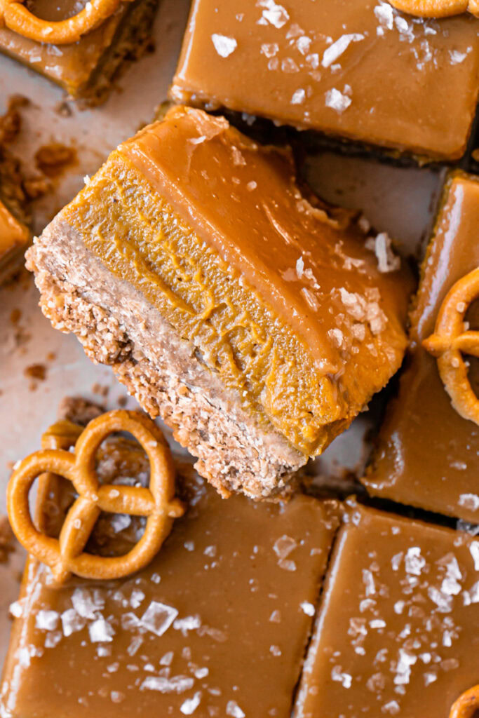 a close up overhead shot of sliced Salted Caramel Pumpkin Pie Bars, the middle one flipped on its side to reveal the pumpkin filling